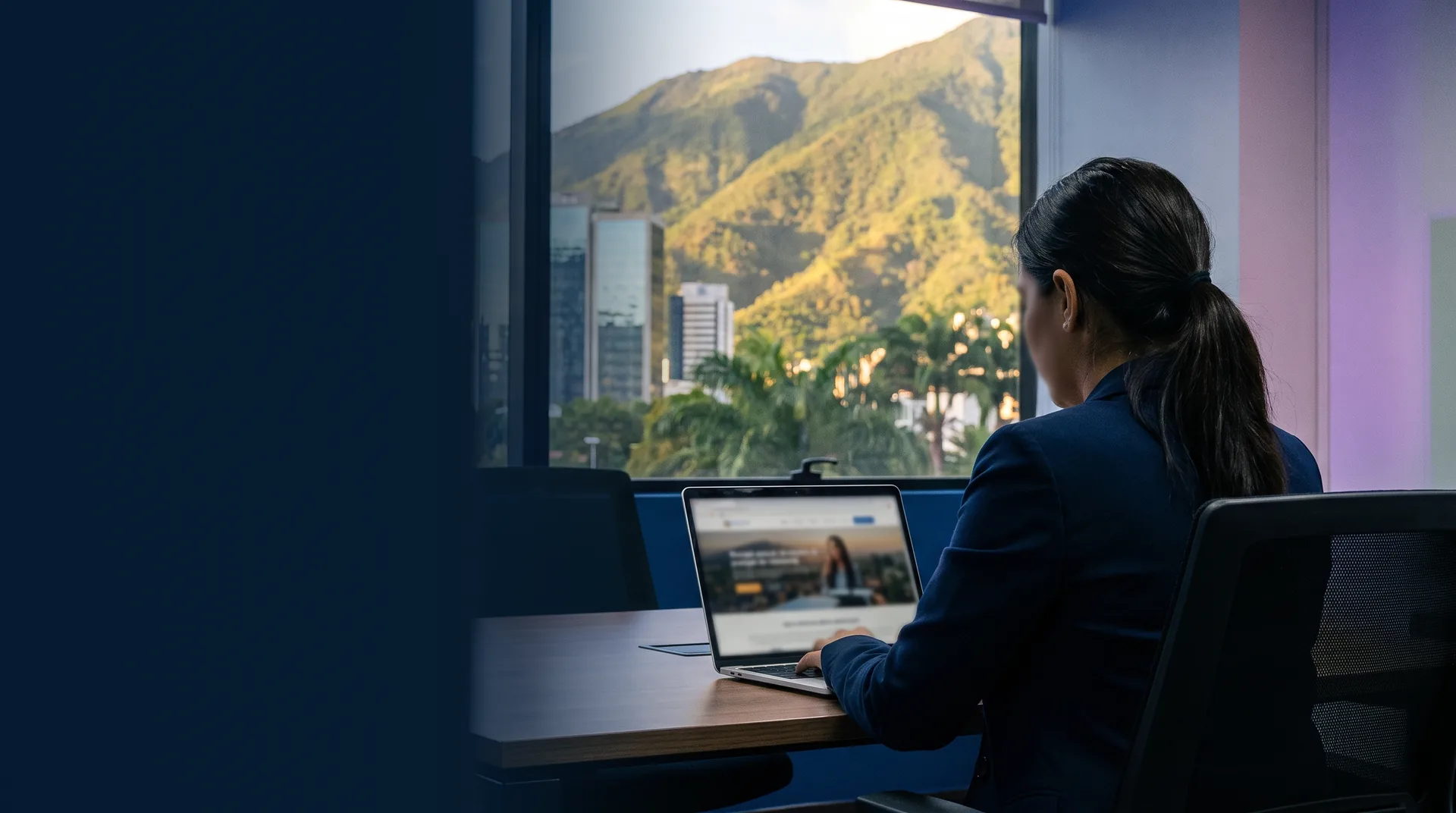 Empresaria de Caracas revisa la página web de su empresa en una laptop, con el cerro El Ávila al fondo